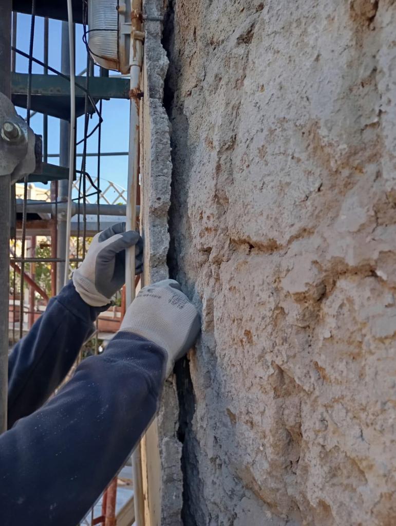 Distacco di intonaco cementizio da muratura in tufo con evidenza del contatto tra materiali incompatibili